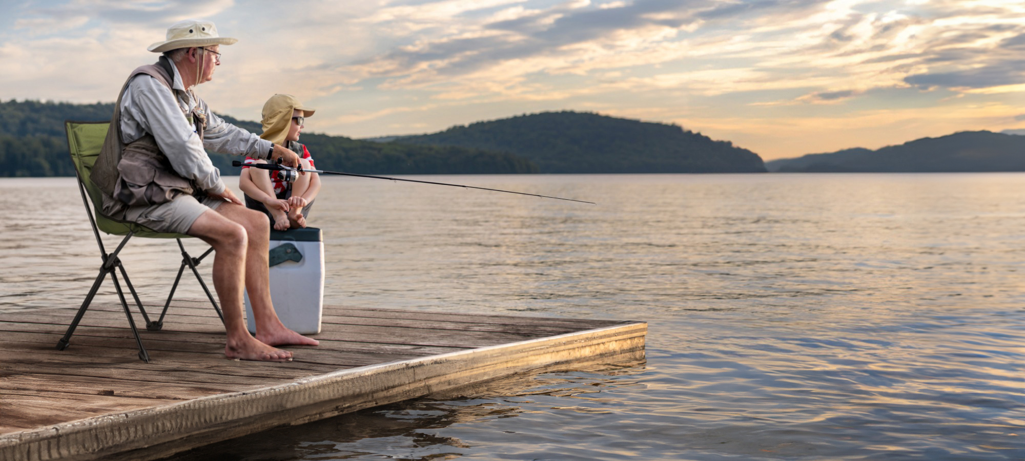 A senior man and a boy are fishing together on a wharf.